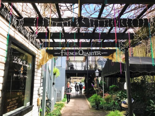A charming pathway leads to the "French Quarter" sign, adorned with colorful beads and greenery.