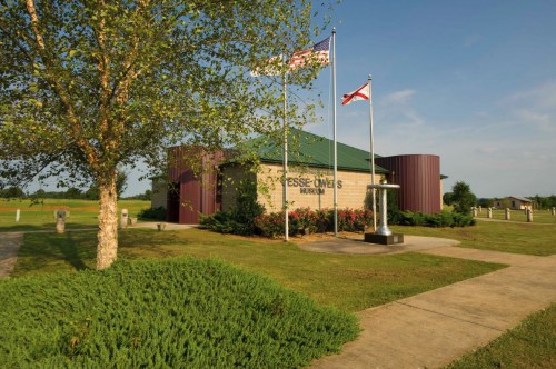 Exterior view of the Jesse Owens Museum, featuring flags and landscaped grounds under a clear blue sky.