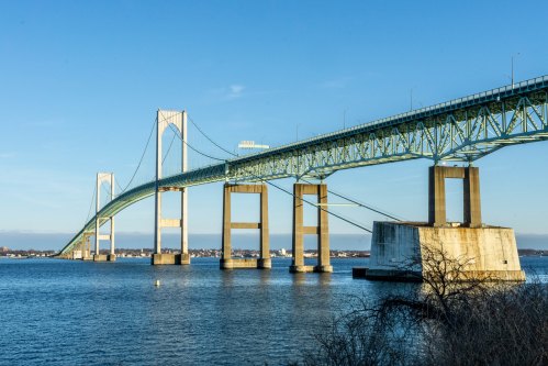 A large suspension bridge spans over a calm body of water under a clear blue sky.