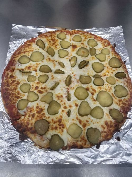 A pizza topped with cheese and numerous pickle slices, cut into triangular slices on a foil-lined surface.