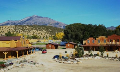 A scenic view of a rustic lodge with wooden buildings, surrounded by mountains and clear blue skies.