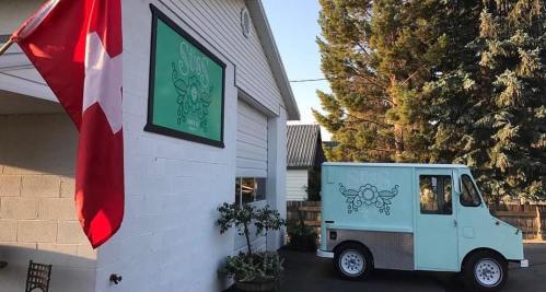A mint green food truck parked beside a building, with a red flag and a decorative sign above it.