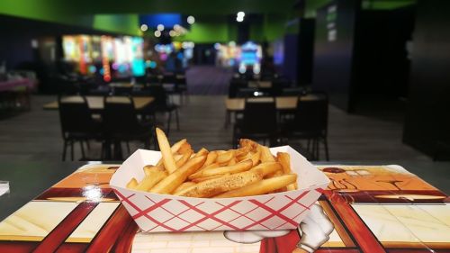 A basket of golden fries sits on a table, with a colorful arcade in the background.