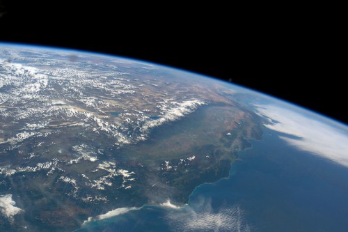 A view of Earth from space, showcasing land, mountains, and ocean with clouds scattered across the surface.
