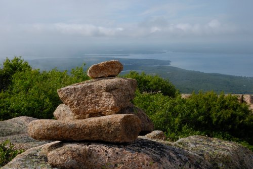 A stack of rocks on a rocky surface, overlooking a lush landscape and a body of water under a cloudy sky.