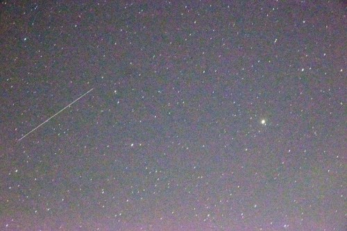A starry night sky with numerous stars and a bright object, possibly a planet, alongside a faint streak of a meteor.