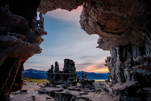 A dramatic landscape featuring unique rock formations against a colorful sky at sunset, framed by rocky arches.