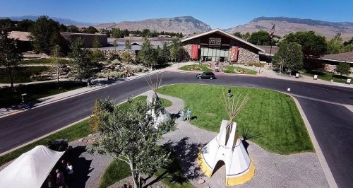 Aerial view of a visitor center with tipis in the foreground, surrounded by greenery and mountains in the background.