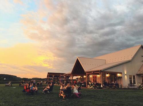 A lively outdoor gathering at a rustic venue during sunset, with people seated and enjoying the scenery.
