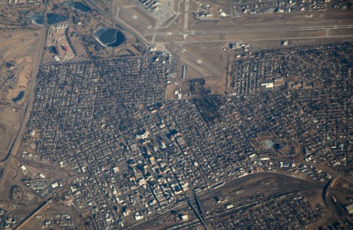 Aerial view of a city with a grid layout, roads, and nearby airport facilities.