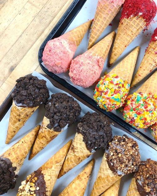 A tray of colorful ice cream cones topped with various toppings, including sprinkles, crushed cookies, and strawberry flakes.