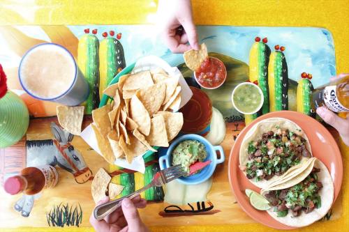 A vibrant table setting with tacos, chips, salsa, guacamole, and drinks, featuring colorful cactus decorations.