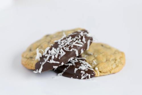 Two cookies stacked, one dipped in chocolate and topped with shredded coconut, on a white background.