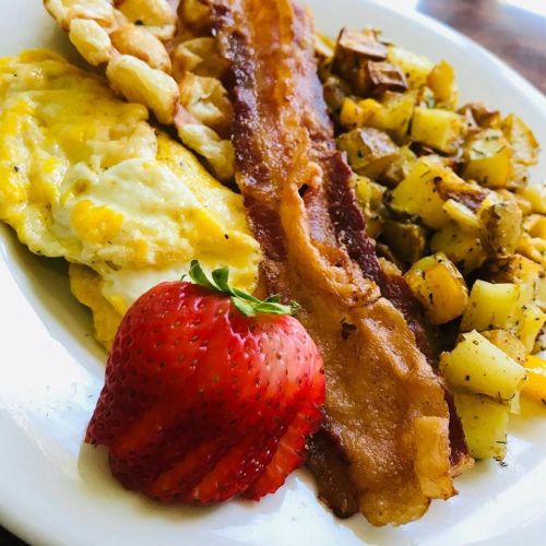 A plate of breakfast featuring an omelet, crispy bacon, seasoned potatoes, and a fresh strawberry.