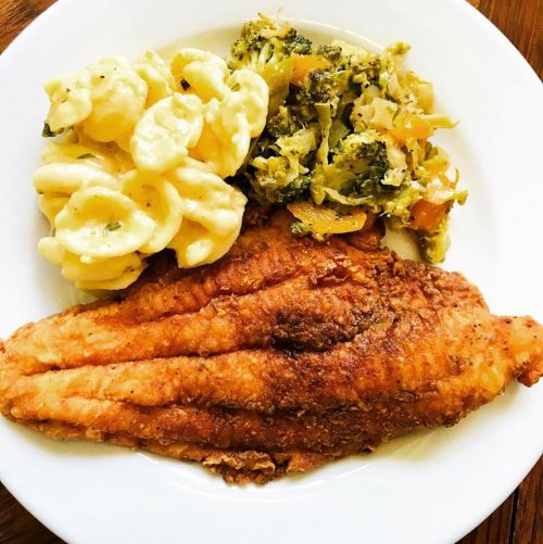 A plate featuring fried fish fillet, macaroni and cheese, and a side of sautéed broccoli and vegetables.