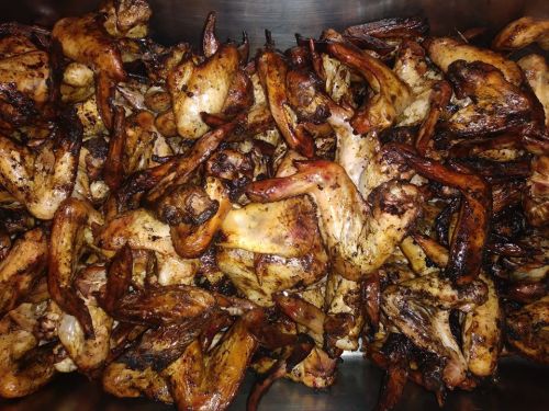 A close-up of a large pile of grilled chicken wings, golden brown and charred, arranged in a metal container.