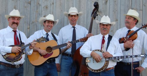 A five-member band in cowboy hats poses with instruments, including a guitar, banjo, mandolin, and violin, against a wooden backdrop.