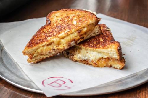 A golden-brown grilled cheese sandwich, cut in half, revealing melted cheese and crispy bread on a silver plate.