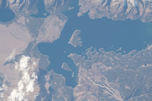 Aerial view of a blue lake surrounded by land, with islands and mountainous terrain in the background.
