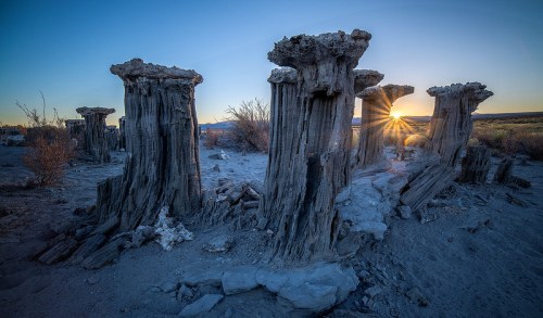 Sunset over unique rock formations in a desert landscape, with rays of light shining through the pillars.