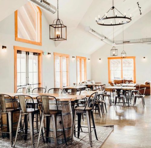 A spacious, modern dining area with wooden tables, metal chairs, and large windows, featuring warm lighting and a cozy atmosphere.