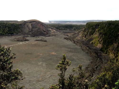 A barren volcanic landscape with steep rocky cliffs and sparse vegetation, under a cloudy sky.