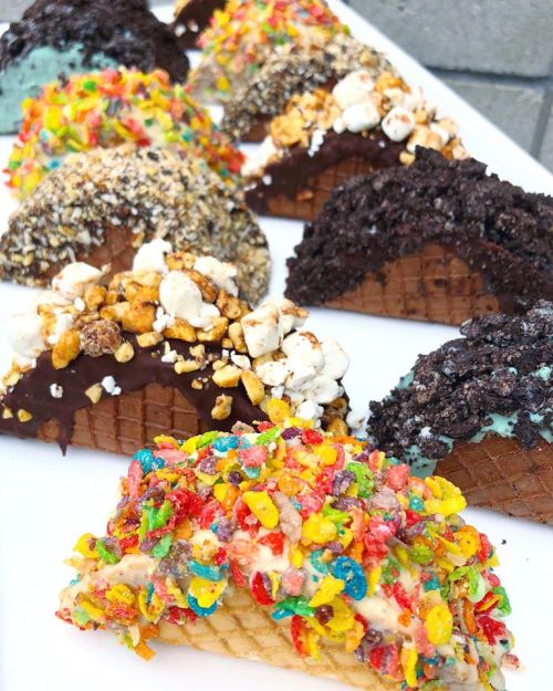 A variety of ice cream tacos with colorful toppings, including chocolate, popcorn, and cereal, displayed on a white plate.