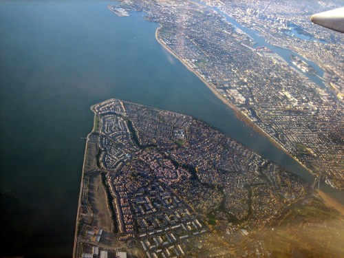 Aerial view of a coastal city with a mix of residential areas and water, showcasing urban development along the shoreline.
