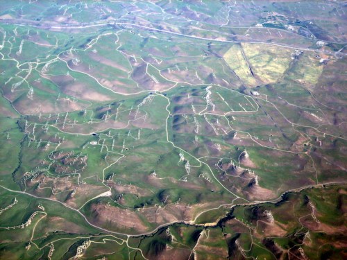 Aerial view of rolling green hills and winding roads, showcasing a patchwork of natural landscapes and terrain.