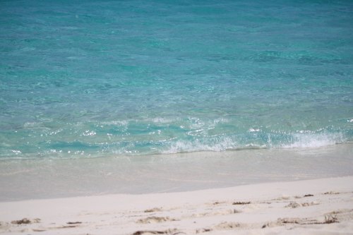 A serene beach scene with clear turquoise water gently lapping at the sandy shore under bright sunlight.