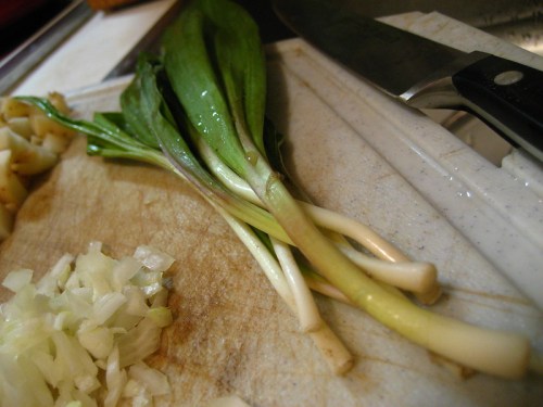 Fresh green onions on a cutting board, with chopped onions and a knife nearby.