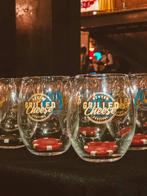 A row of clear glasses with a grilled cheese festival logo, placed on a black tablecloth with poker chips.