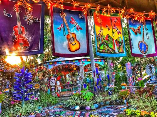 Colorful banners featuring musical instruments and nature hang in a vibrant garden filled with plants and artistic decorations.