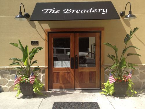 Entrance of The Breadery featuring wooden double doors, potted plants, and small American flags.