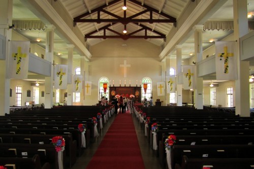 Interior of a church with rows of pews, a red carpet, and decorative banners featuring crosses.