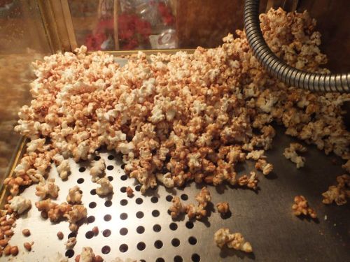 A close-up of freshly popped popcorn spilling out of a popcorn machine onto a metal surface.