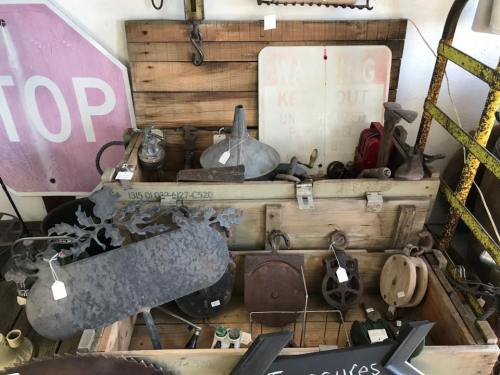 A collection of vintage tools and decor items displayed in a wooden crate, including a funnel, wheels, and metal signs.