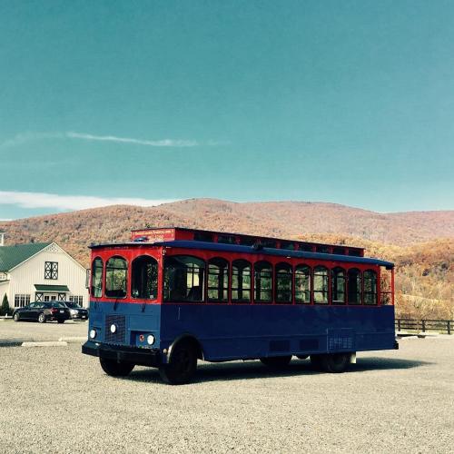 A vintage-style blue and red trolley parked in a gravel lot with autumn mountains in the background.
