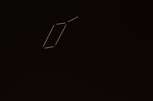 A dark night sky featuring a constellation outlined in yellow, with a bright star at one end.