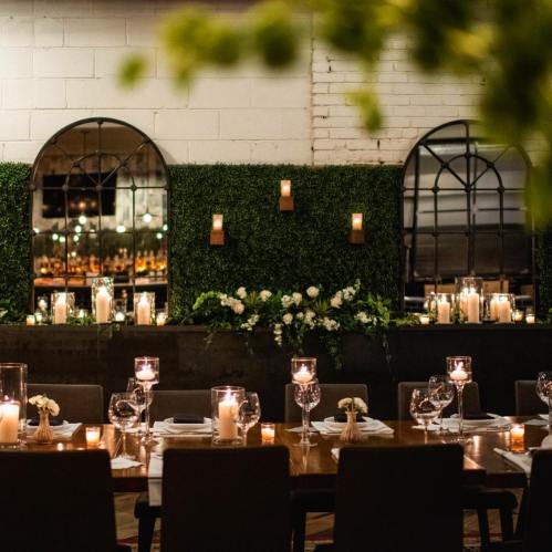 A beautifully set dining table with candles and floral decor in a cozy, greenery-adorned restaurant interior.