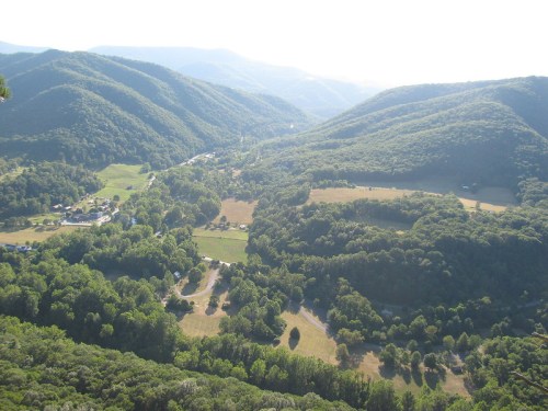 A panoramic view of lush green mountains and valleys under a bright sky, showcasing a serene rural landscape.