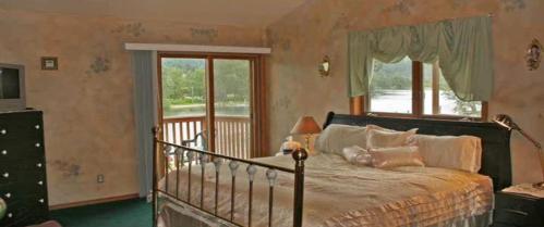 Cozy bedroom with a large bed, dresser, and windows overlooking a scenic lake view. Soft colors and decor create a warm atmosphere.