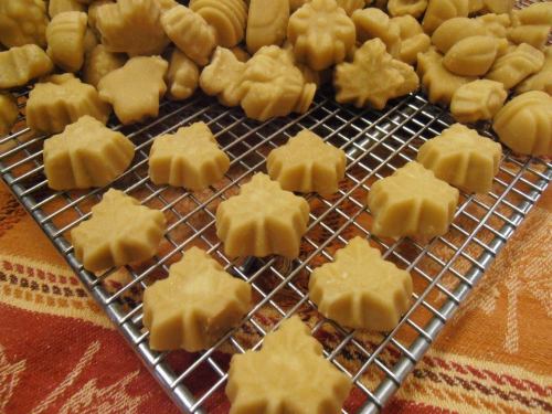 A cooling rack filled with various shaped, light brown candies, including leaves and other decorative forms.