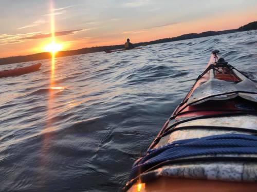 A kayak on water at sunset, with a person paddling in the distance and vibrant colors in the sky.