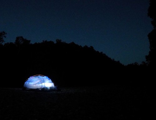 A glowing tent set against a dark night sky, surrounded by trees and stars.