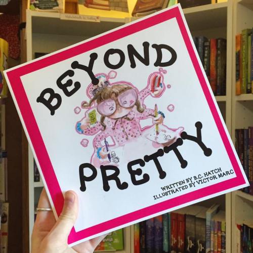 A person holds a colorful children's book titled "Beyond Pretty," featuring a whimsical illustration on the cover.