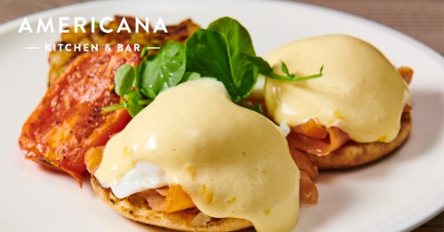 Two eggs Benedict with smoked salmon on English muffins, topped with hollandaise sauce and garnished with greens.