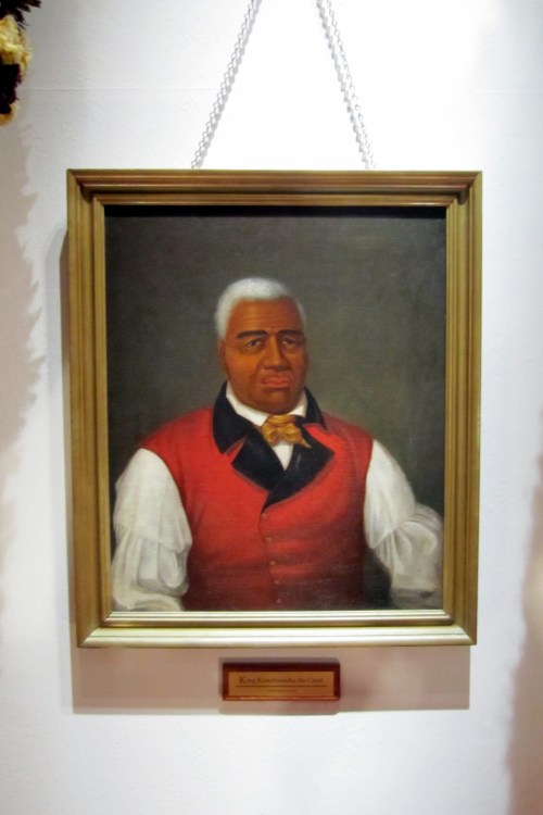 Portrait of a man with gray hair, wearing a red vest and white shirt, framed and displayed on a wall.