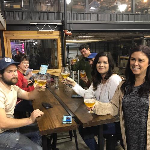 A group of friends enjoying drinks at a brewery, smiling and toasting with large glasses of beer.