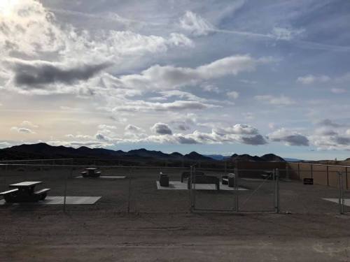 A fenced area with picnic tables and mountains in the background under a cloudy sky.